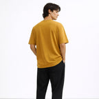 Person wearing a mustard yellow t-shirt and black pants on a white background