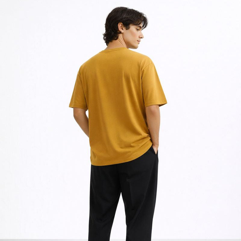 Person wearing a mustard yellow t-shirt and black pants on a white background
